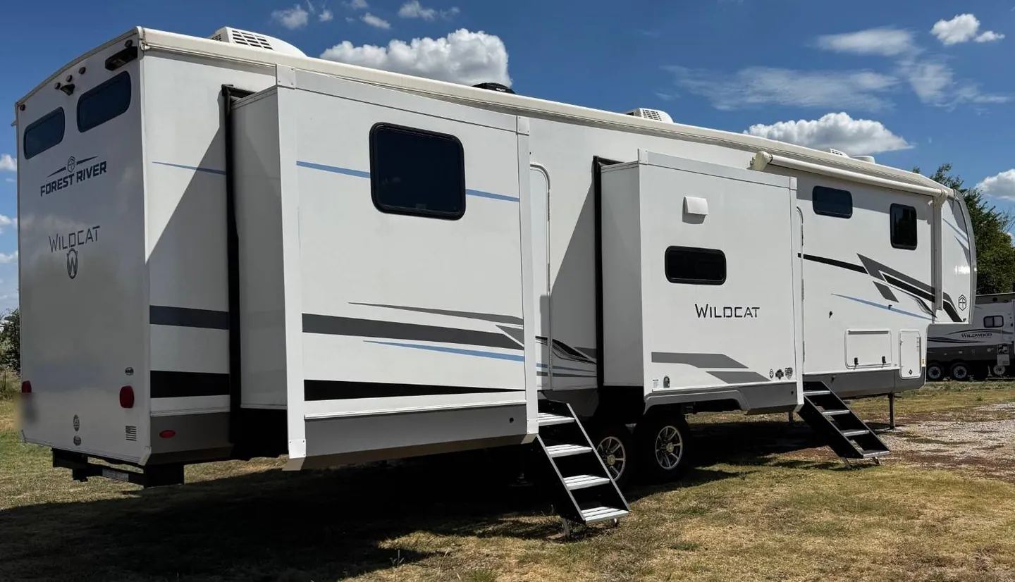 A Forest River Wildcat fifth-wheel trailer set up on grass with its slide-outs open and steps down